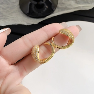 Detailed view of hand-held gold C-shape earrings with pave cubic zirconia settings