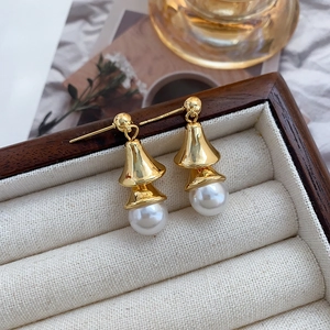 Detailed shot of gold-plated bell-shaped pearl earrings on a premium fabric display tray