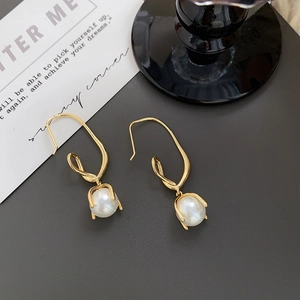 Macro detail of gold-plated knot earrings with glossy white round pearls on grey stone