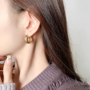 Polished gold circular hoop earrings with intricate woven texture shown on a model