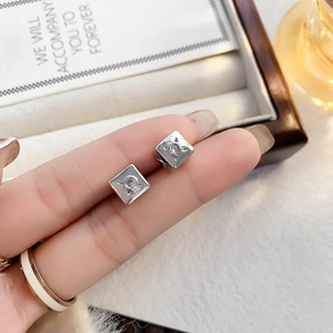 Gros plan sur des boucles d'oreilles carrées en argent avec zircon tenues entre les doigts