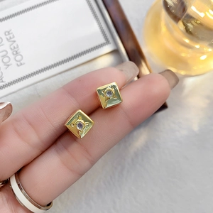 Détail d'une boucle d'oreille carrée dorée avec zircon violet tenue par les doigts