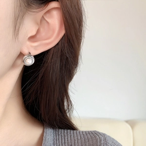 Elegant pearl stud earrings with circular silver metal base worn by a model in soft light