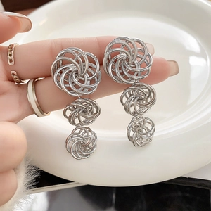 Detailed view of silver triple-layered hollow swirl drop earrings held by hand