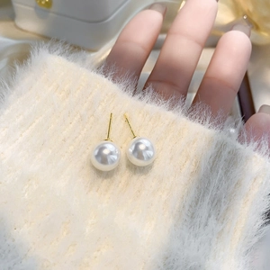 Gros plan de boucles d'oreilles perles blanches avec tiges dorées sur un pull doux