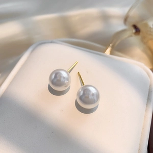 Élégantes boucles d'oreilles perles rondes plaquées or sur un support blanc texturé