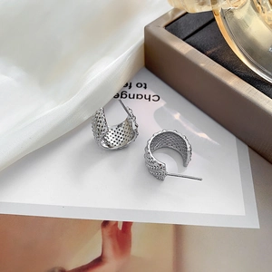 Fashionable C-shaped silver hollow hoop earrings with textured mesh on white silk background