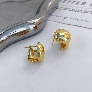 Macro detail of high-polish geometric gold-plated dome earrings on a silver tray