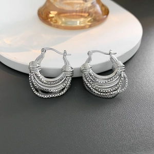 Close-up of layered silver U-chain drop earrings on a white display stand