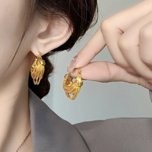 Detail of gold-plated U-shaped fringe earrings worn by a model in soft lighting
