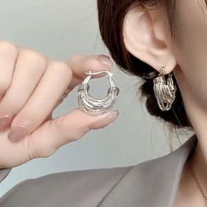 Detailed close-up of woven silver hoop earrings with intricate multi-layer metal texture