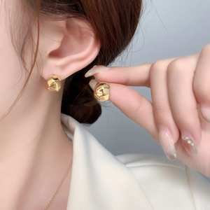 Close-up of geometric faceted C-shaped gold stud earrings worn on model's ear