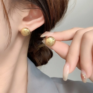 Close-up of golden dome stud earrings featuring a textured granular matte surface