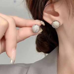 Close-up of minimalist champagne gold ball stud earrings with a fine frosted texture finish