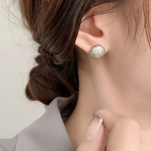 Minimalist silver round stud earrings with a textured sparkling surface on a model