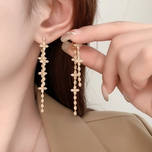 Detail of long gold-plated clover tassel earrings with sparkling zircon stones
