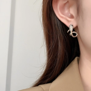 Detailed view of snake-shaped gold stud earrings with cubic zirconia on a female model