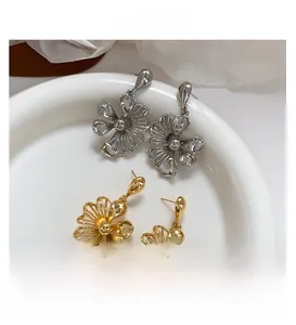 Detail showing elegant gold and silver hollow flower drop earrings on a white tray