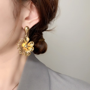 Detailed view of model wearing large golden flower petal drop earrings with metallic luster