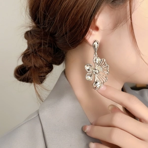 Close-up of minimalist silver floral earrings worn by a model in a grey suit