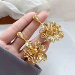 Macro shot of gold flower earrings held by hand showing exquisite hollow petals and shine