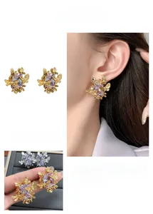 Détail de boucles d'oreilles dorées avec pierre violette et motif de papillon