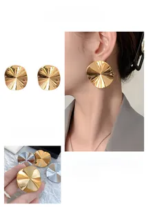 Detailed macro view of large round wavy metal stud earrings in gold and silver finish
