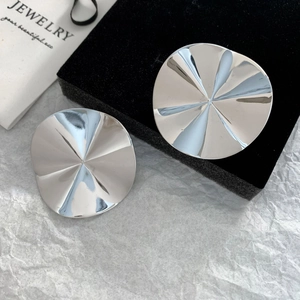 Macro detail of round silver pleated earrings with radial texture on a velvet stand