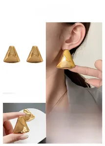 Detailed macro view of large golden triangular stud earrings with diagonal groove texture