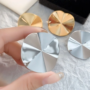 Macro shot of large gold and silver wavy disc earrings showing polished metal texture