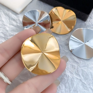 Macro detail of large gold and silver pleated metal earrings with radial folding design