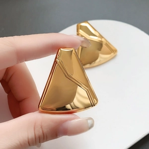 Detail of mirror-polished gold-plated geometric triangle earrings held by hand