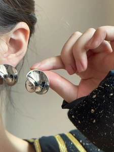 Detalle de pendientes plateados con forma irregular curva y acabado metálico pulido