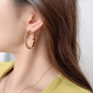 Gros plan de créoles dorées texturées avec des accents scintillants portées par un mannequin
