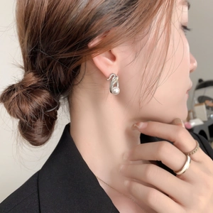 Close-up of elegant silver twisted knot pearl earrings worn by a model in black suit