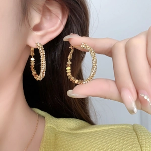 Détail de grandes boucles d'oreilles créoles dorées avec micro-pavage de cristaux