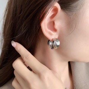 Gros plan d'une boucle d'oreille créole en argent poli sur mannequin au style minimaliste