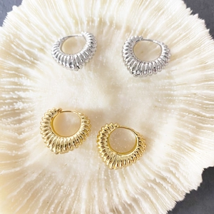 Pair of gold and silver croissant dome hoop earrings on a textured white surface