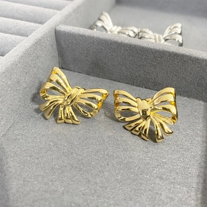 Polished gold bow earrings with a 3D hollow design on a gray velvet jewelry box display