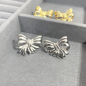 Close-up of polished silver and gold ribbon bow stud earrings on a velvet display tray
