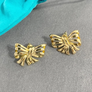 Detail of elegant gold hollow bow stud earrings on a textured grey and teal backdrop