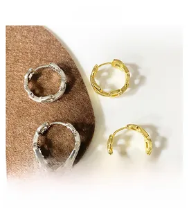 Detail view of gold and silver hoop earrings with chain texture on a soft brown surface
