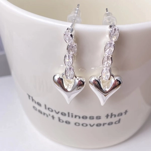 Silver heart drop earrings with marquise-cut crystals hanging on a white ceramic cup