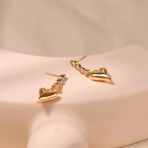 Close-up of heart-shaped gold-plated earrings with clear zircon stones on display