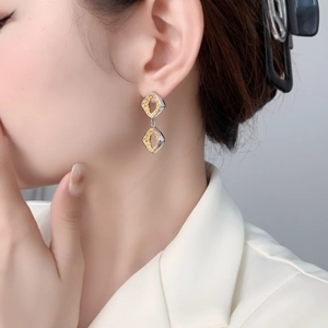 Close-up of geometric hollow diamond-shaped earrings in two-tone gold and silver finish