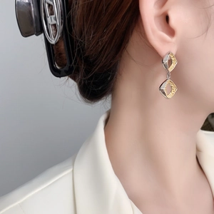 Detail shot of hollow geometric diamond earrings featuring gold textured inlay on metal