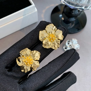 Gros plan sur des boucles d'oreilles fleurs dorées à cinq pétales tenues à la main