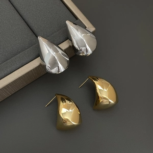 Close-up of minimalist teardrop earrings and gold curved studs on a grey display
