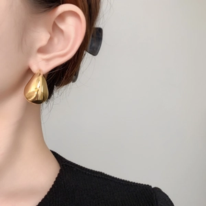 Close-up of polished gold teardrop stud earring worn by model with mirror finish