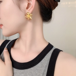 Gros plan d'une boucle d'oreille fleur dorée texturée portée par un mannequin